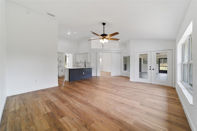 unfurnished living room featuring lofted ceiling, french doors, sink, light hardwood / wood-style flooring, and ceiling fan