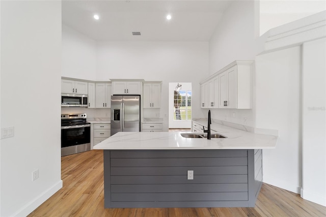 kitchen with kitchen peninsula, appliances with stainless steel finishes, a towering ceiling, sink, and light hardwood / wood-style flooring