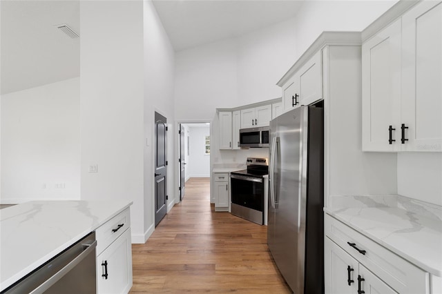 kitchen with white cabinets, light hardwood / wood-style floors, light stone countertops, and stainless steel appliances