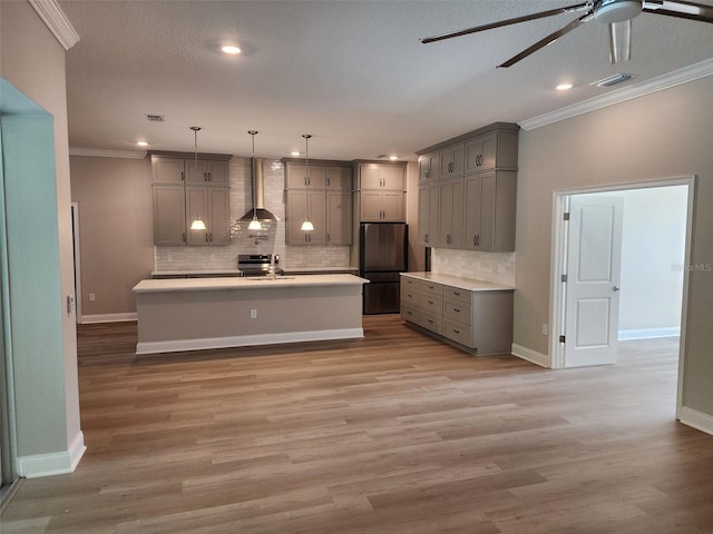 kitchen featuring pendant lighting, a center island with sink, wall chimney range hood, stainless steel fridge, and light hardwood / wood-style floors