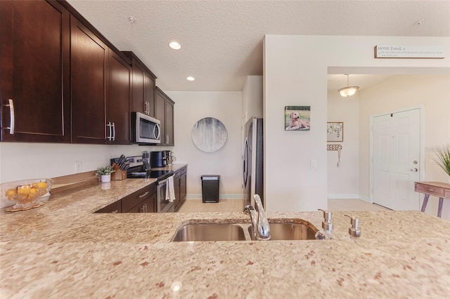 kitchen with sink, appliances with stainless steel finishes, decorative light fixtures, light stone counters, and dark brown cabinetry