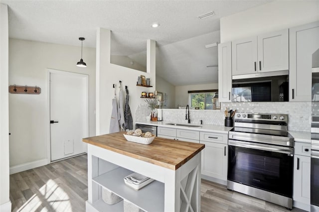 kitchen with appliances with stainless steel finishes, vaulted ceiling, sink, decorative light fixtures, and white cabinetry