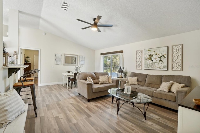 living room with a textured ceiling, ceiling fan, lofted ceiling, and light wood-type flooring