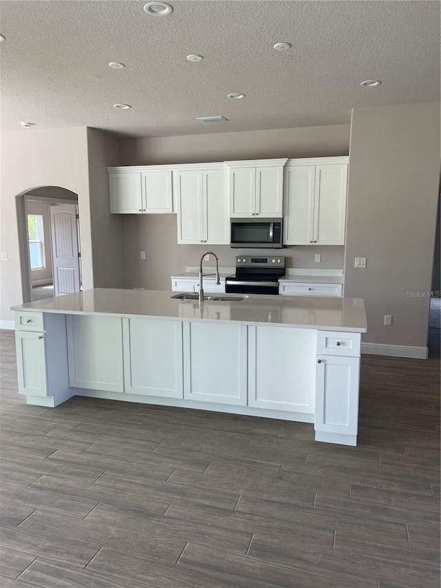 kitchen featuring appliances with stainless steel finishes, sink, white cabinets, a kitchen island with sink, and a textured ceiling