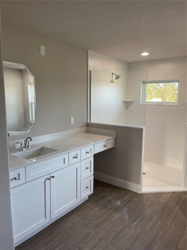 bathroom featuring wood-type flooring, vanity, a textured ceiling, and a tile shower