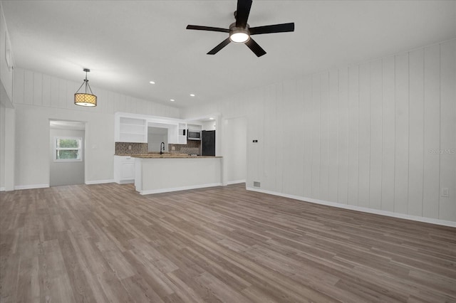 unfurnished living room featuring ceiling fan, sink, wooden walls, and hardwood / wood-style flooring