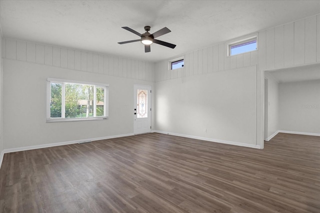 unfurnished living room featuring a textured ceiling, dark hardwood / wood-style flooring, ceiling fan, and wood walls