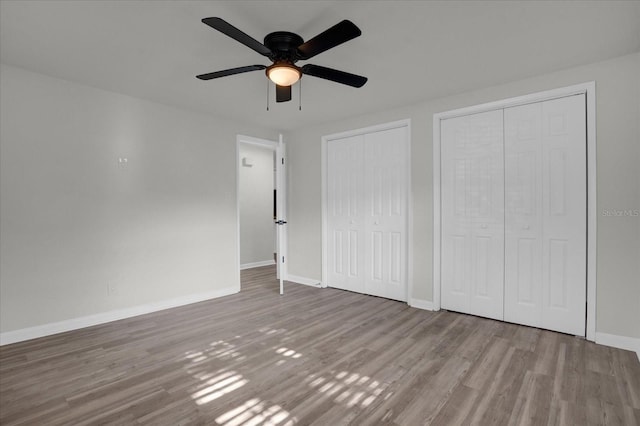 unfurnished bedroom with two closets, light hardwood / wood-style floors, and ceiling fan