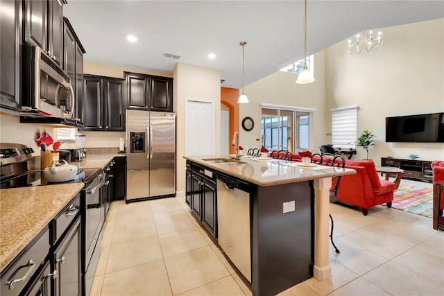 kitchen with a kitchen island with sink, hanging light fixtures, sink, light stone countertops, and appliances with stainless steel finishes