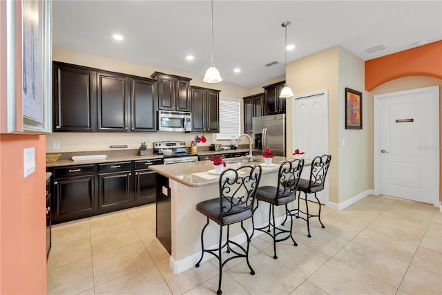 kitchen with sink, light stone counters, decorative light fixtures, a center island with sink, and appliances with stainless steel finishes