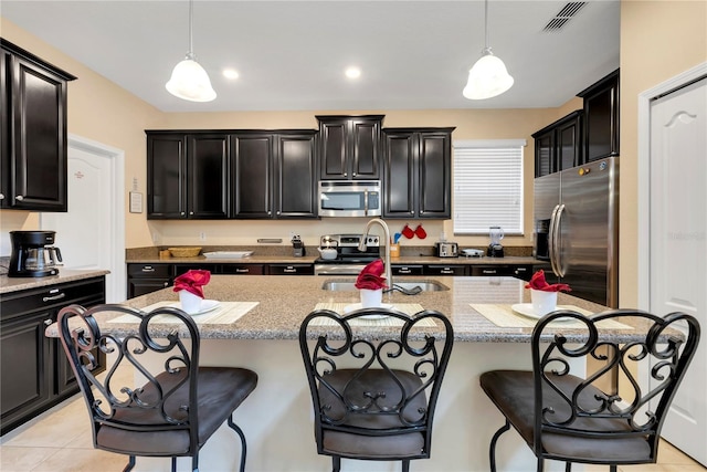 kitchen with a center island with sink, hanging light fixtures, and appliances with stainless steel finishes