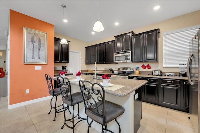 kitchen with a kitchen bar, light stone counters, stainless steel appliances, pendant lighting, and a center island with sink