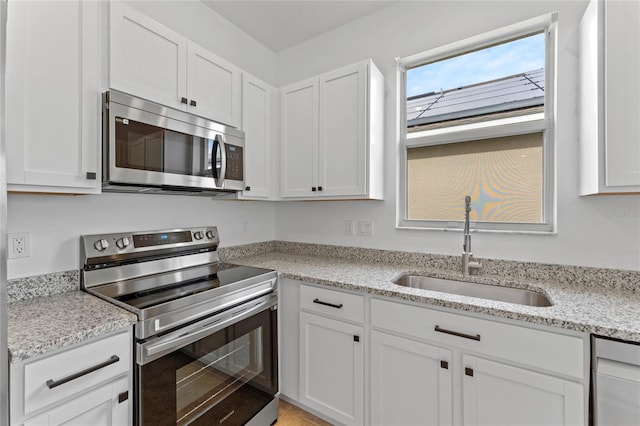 kitchen with light stone countertops, appliances with stainless steel finishes, white cabinets, and sink