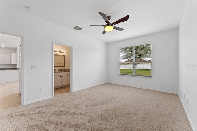 unfurnished bedroom with ceiling fan, light colored carpet, ensuite bath, a walk in closet, and a closet