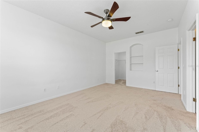 unfurnished bedroom with ceiling fan, light carpet, a closet, and a walk in closet