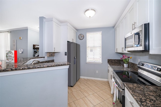 kitchen featuring kitchen peninsula, stainless steel appliances, white cabinetry, and dark stone counters