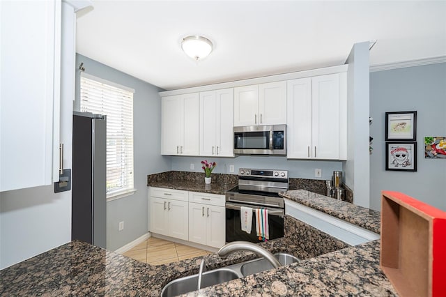 kitchen with sink, light tile patterned flooring, dark stone countertops, white cabinets, and appliances with stainless steel finishes