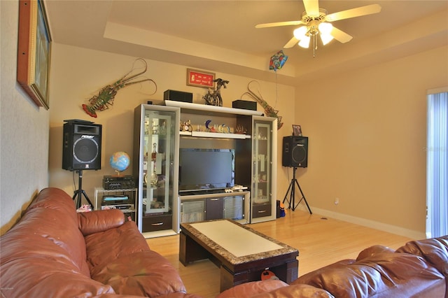 living room with wood-type flooring, a tray ceiling, and ceiling fan