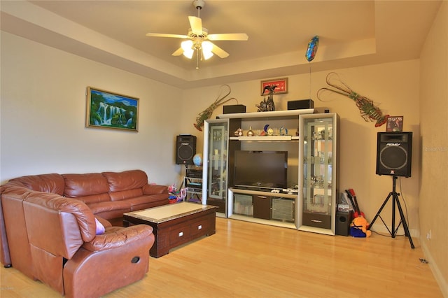 living room featuring light wood-type flooring, a tray ceiling, and ceiling fan