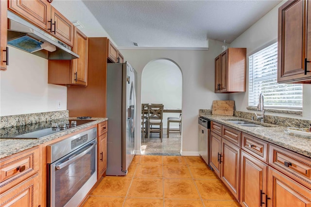 kitchen with sink, light tile patterned floors, a textured ceiling, light stone counters, and stainless steel appliances