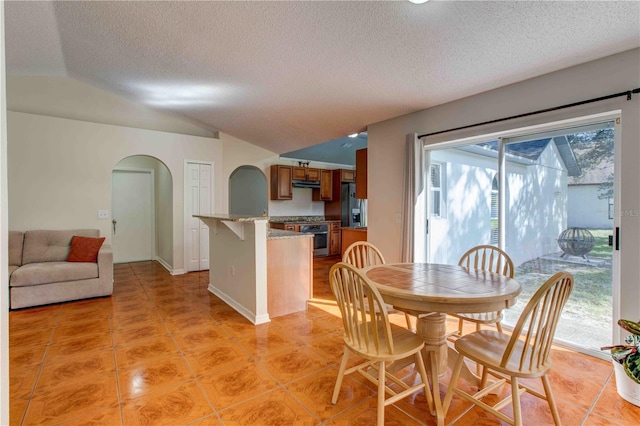 dining space featuring vaulted ceiling, light tile patterned flooring, and a textured ceiling