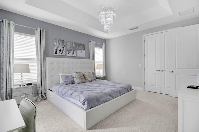 carpeted bedroom with a raised ceiling, a closet, and a notable chandelier