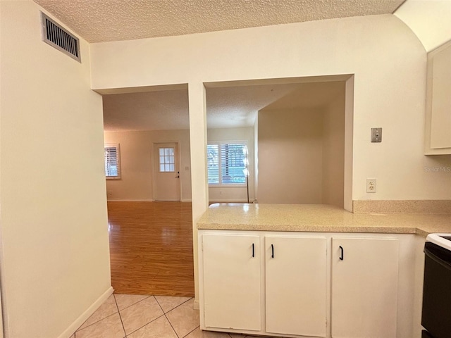 kitchen with white cabinets, electric range oven, light wood-type flooring, and a textured ceiling