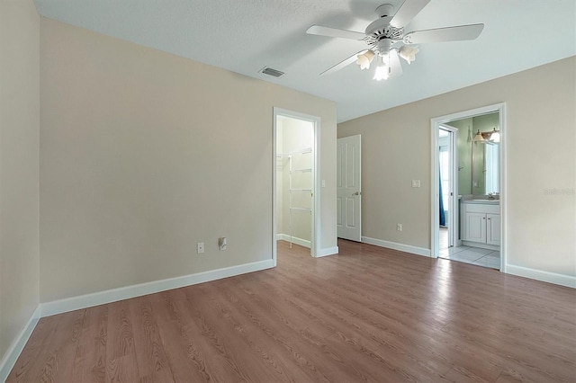 unfurnished bedroom featuring a walk in closet, ensuite bathroom, a closet, and light wood-type flooring