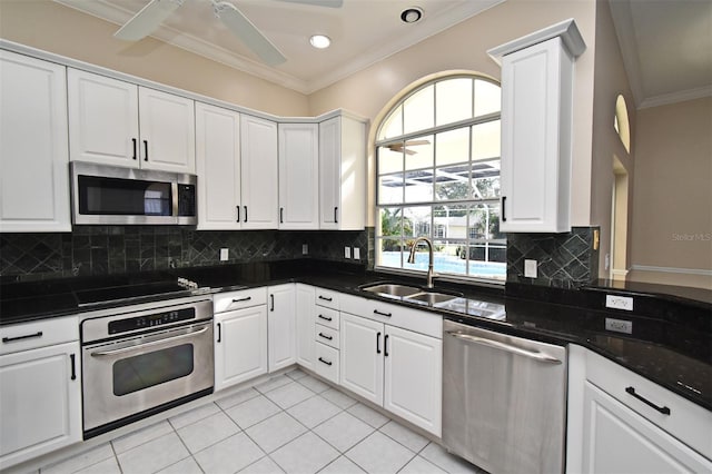 kitchen featuring appliances with stainless steel finishes, sink, white cabinets, dark stone counters, and crown molding