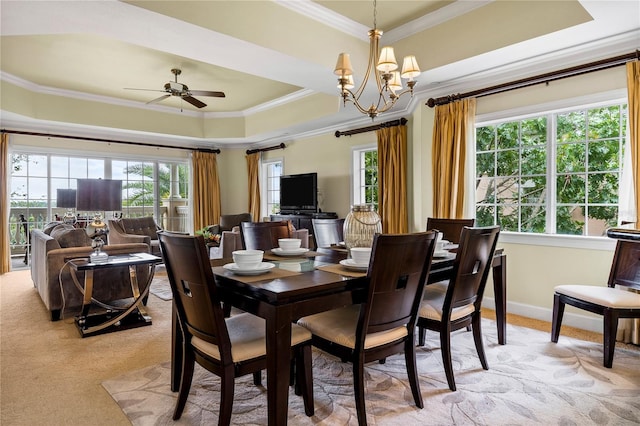 carpeted dining space with ceiling fan with notable chandelier, a healthy amount of sunlight, a raised ceiling, and crown molding