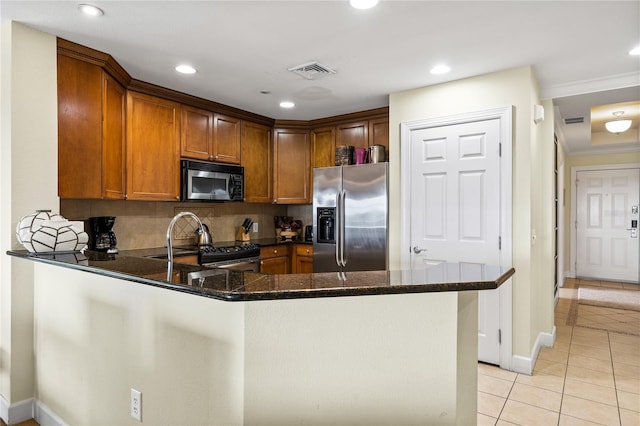 kitchen featuring kitchen peninsula, decorative backsplash, stainless steel appliances, light tile patterned floors, and dark stone countertops