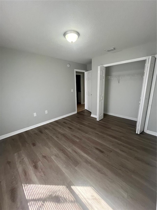 unfurnished bedroom featuring a textured ceiling, dark wood-type flooring, and a closet