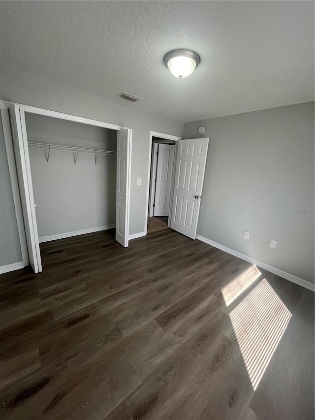 unfurnished bedroom featuring a textured ceiling, a closet, and dark hardwood / wood-style floors