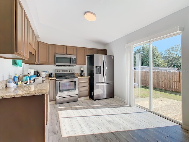 kitchen with light stone countertops, sink, stainless steel appliances, vaulted ceiling, and light wood-type flooring