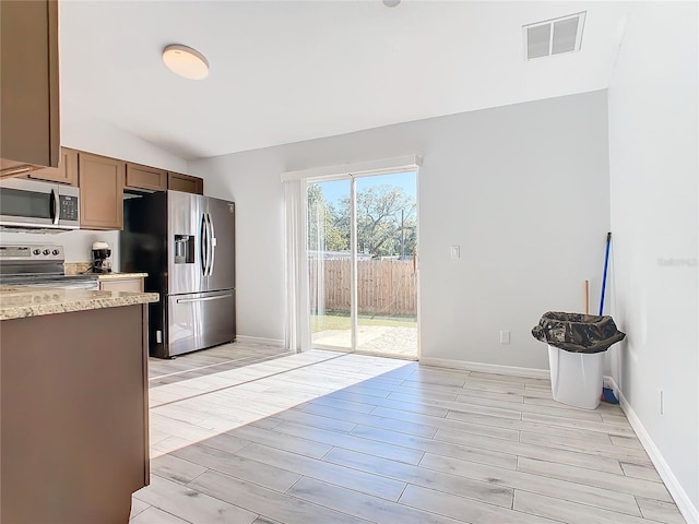 kitchen featuring vaulted ceiling, light stone countertops, appliances with stainless steel finishes, and light hardwood / wood-style flooring