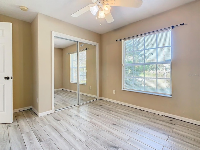 unfurnished bedroom featuring ceiling fan, a closet, light hardwood / wood-style floors, and multiple windows