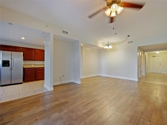 unfurnished living room with ceiling fan with notable chandelier and light hardwood / wood-style floors