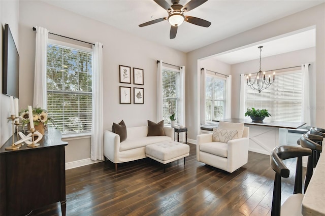 living area with ceiling fan with notable chandelier, dark wood-type flooring, and a wealth of natural light