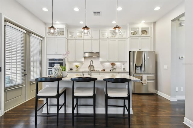 kitchen featuring stainless steel fridge, dark hardwood / wood-style flooring, pendant lighting, white cabinets, and an island with sink