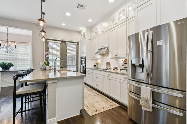 kitchen with white cabinetry, dark wood-type flooring, stainless steel appliances, pendant lighting, and a center island with sink