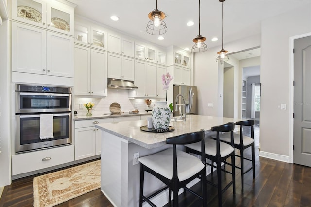 kitchen with appliances with stainless steel finishes, dark hardwood / wood-style flooring, pendant lighting, and an island with sink