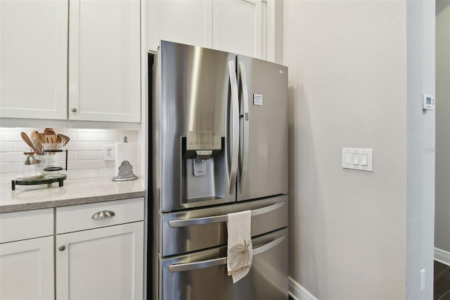 kitchen featuring backsplash, light stone counters, white cabinets, and stainless steel refrigerator with ice dispenser