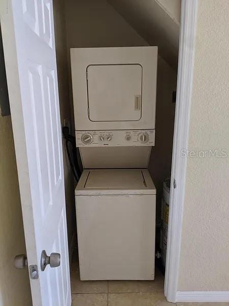 laundry area with stacked washer / dryer and light tile patterned flooring