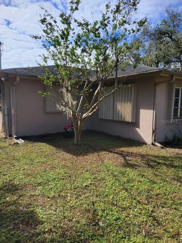 view of side of property with roof with shingles, a lawn, and stucco siding