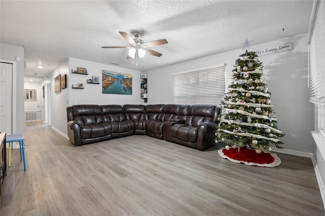 living room with light hardwood / wood-style floors, ceiling fan, and a textured ceiling