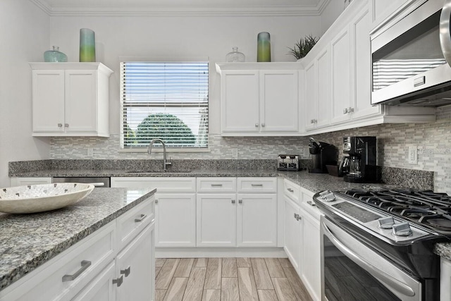 kitchen with appliances with stainless steel finishes, backsplash, crown molding, sink, and white cabinetry