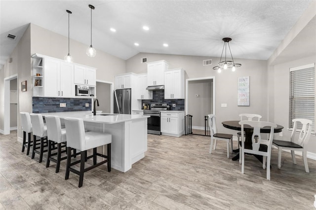 kitchen featuring appliances with stainless steel finishes, sink, white cabinets, hanging light fixtures, and an island with sink