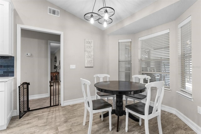 dining space featuring lofted ceiling, light hardwood / wood-style floors, and a notable chandelier