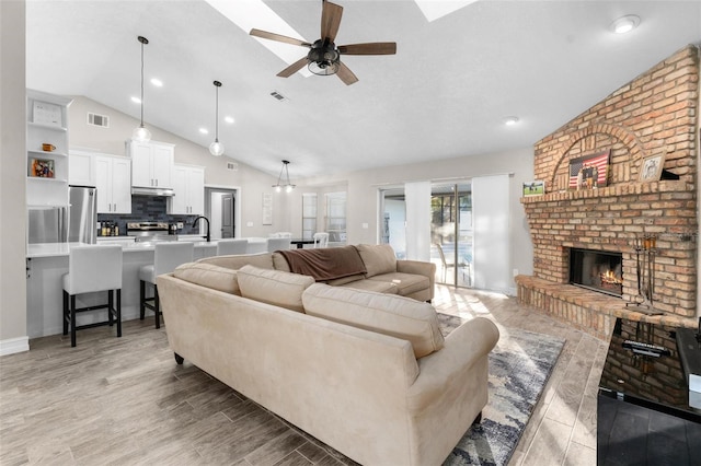 living room with ceiling fan, light hardwood / wood-style floors, lofted ceiling, and a brick fireplace