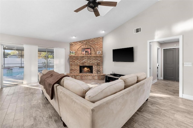 living room featuring a brick fireplace, ceiling fan, high vaulted ceiling, and light wood-type flooring